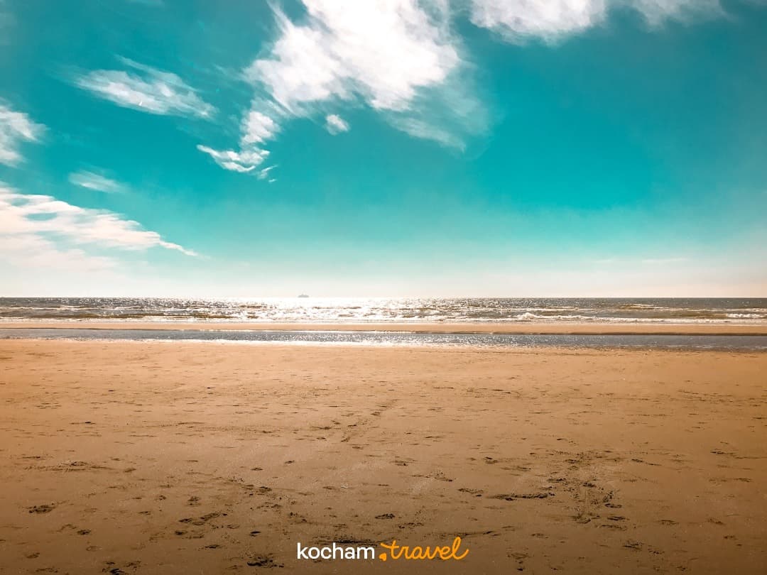 Słoneczna, piaszczysta plaża, morze i błękitne niebo z chmurami.