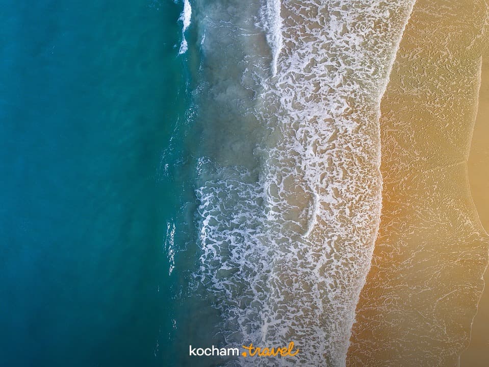 Widok z lotu ptaka: turkusowy ocean, piaszczysta plaża, białe fale.
