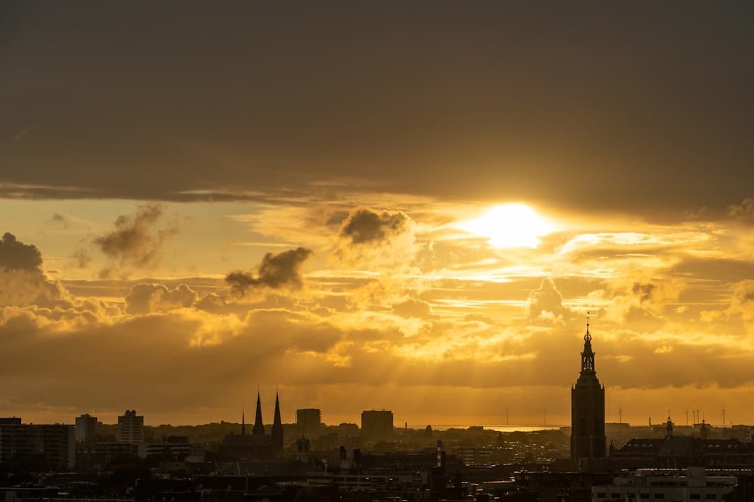 Panorama miasta o zachodzie słońca, złote chmury, sylwetki budynków.