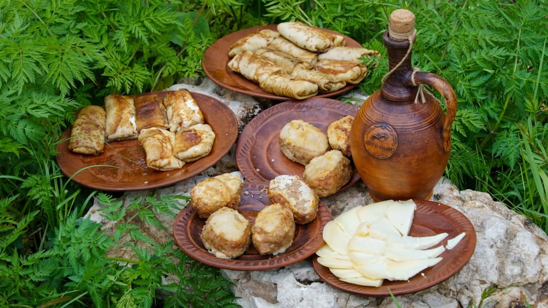 Rustykalny posiłek na świeżym powietrzu: naleśniki, ser, pieczone dania, gliniany dzbanek.