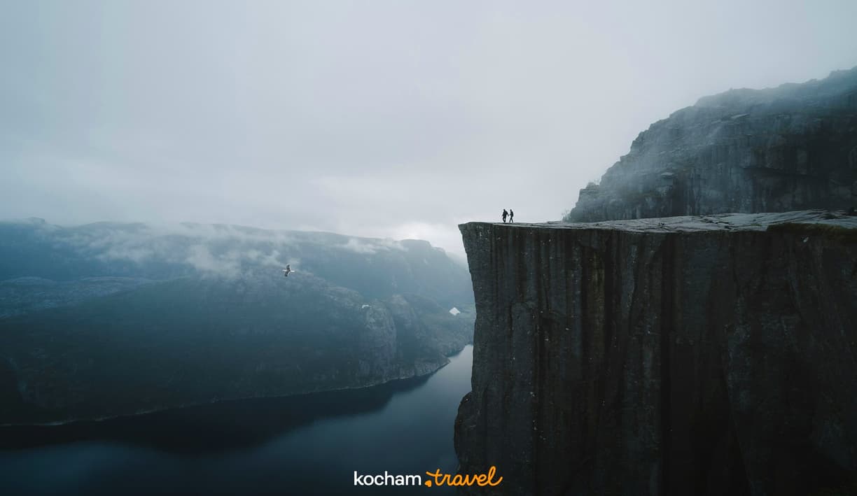 Dwoje ludzi na klifie Preikestolen, mglisty norweski fiord.