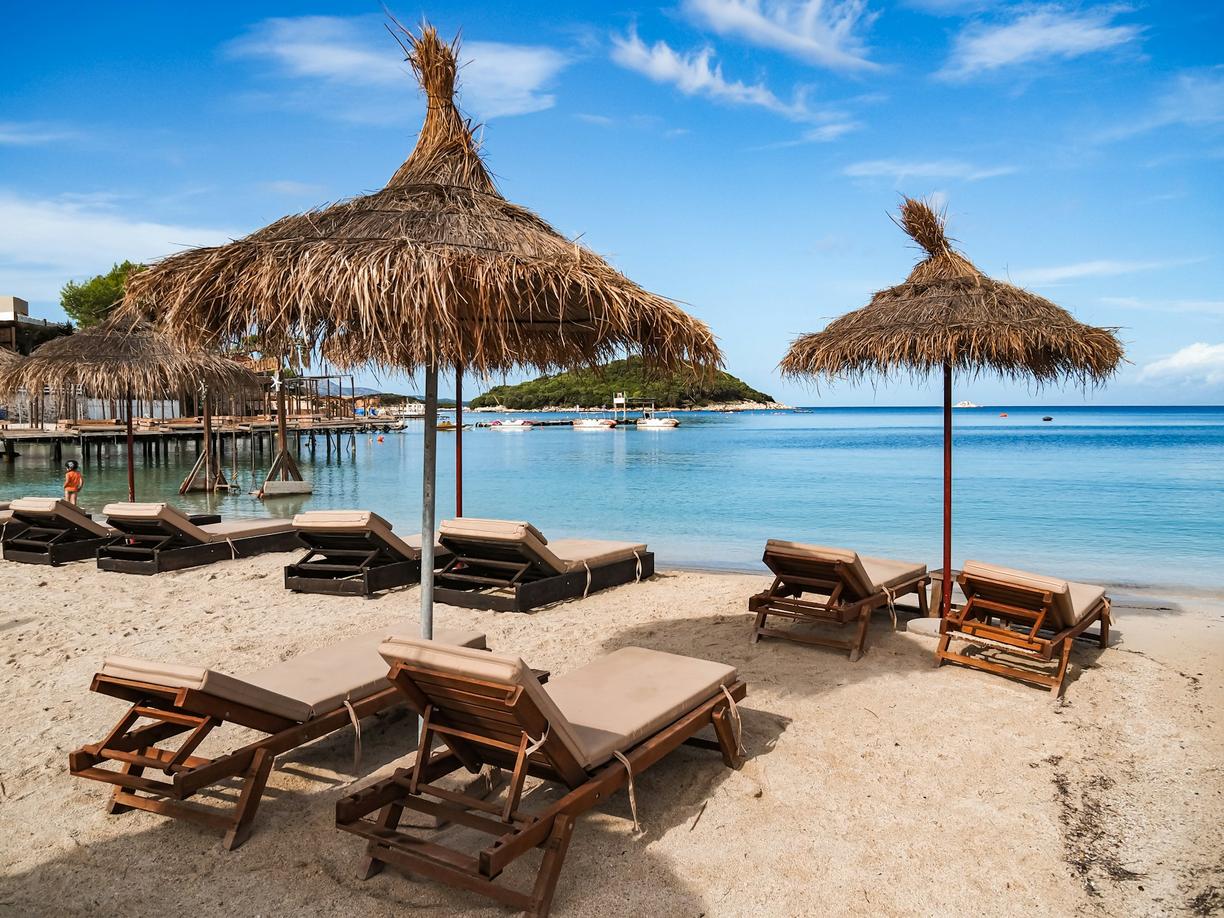 Wakacyjny kurort z piaszczystą plażą, leżakami i słomianymi parasolami.