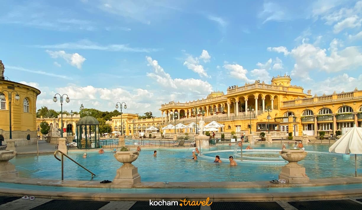 Kąpielisko termalne Szechenyi w Budapeszcie, żółte budynki, relaksujący się ludzie.