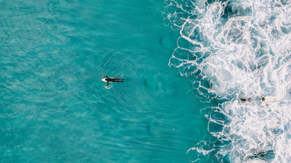 Surferzy na deskach w turkusowym oceanie obok spienionych fal
