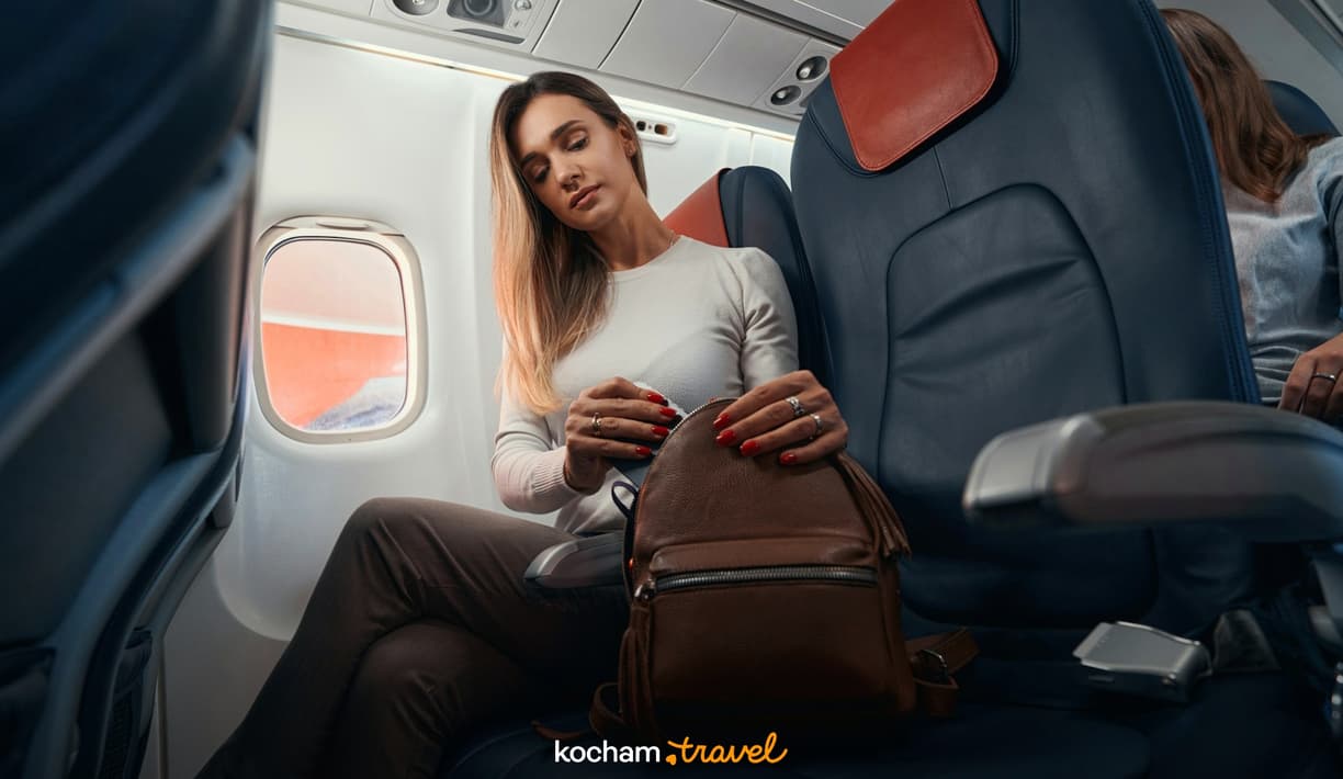Kobieta otwiera plecak podręczny w fotelu samolotu.