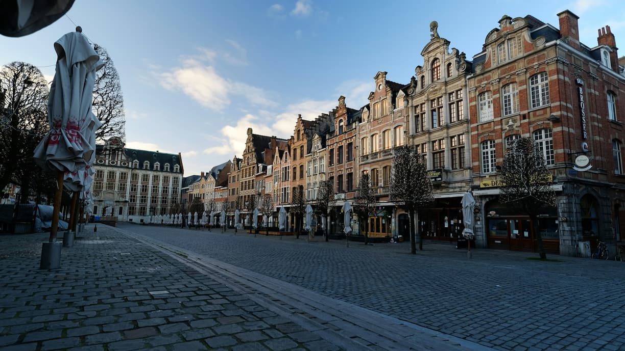 Pusty brukowany plac z zabytkowymi kamienicami i złożonymi parasolami.