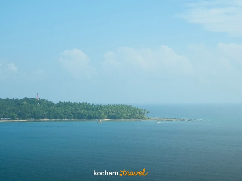 Tropikalna wyspa z latarnią morską, turkusowy ocean, błękitne niebo.