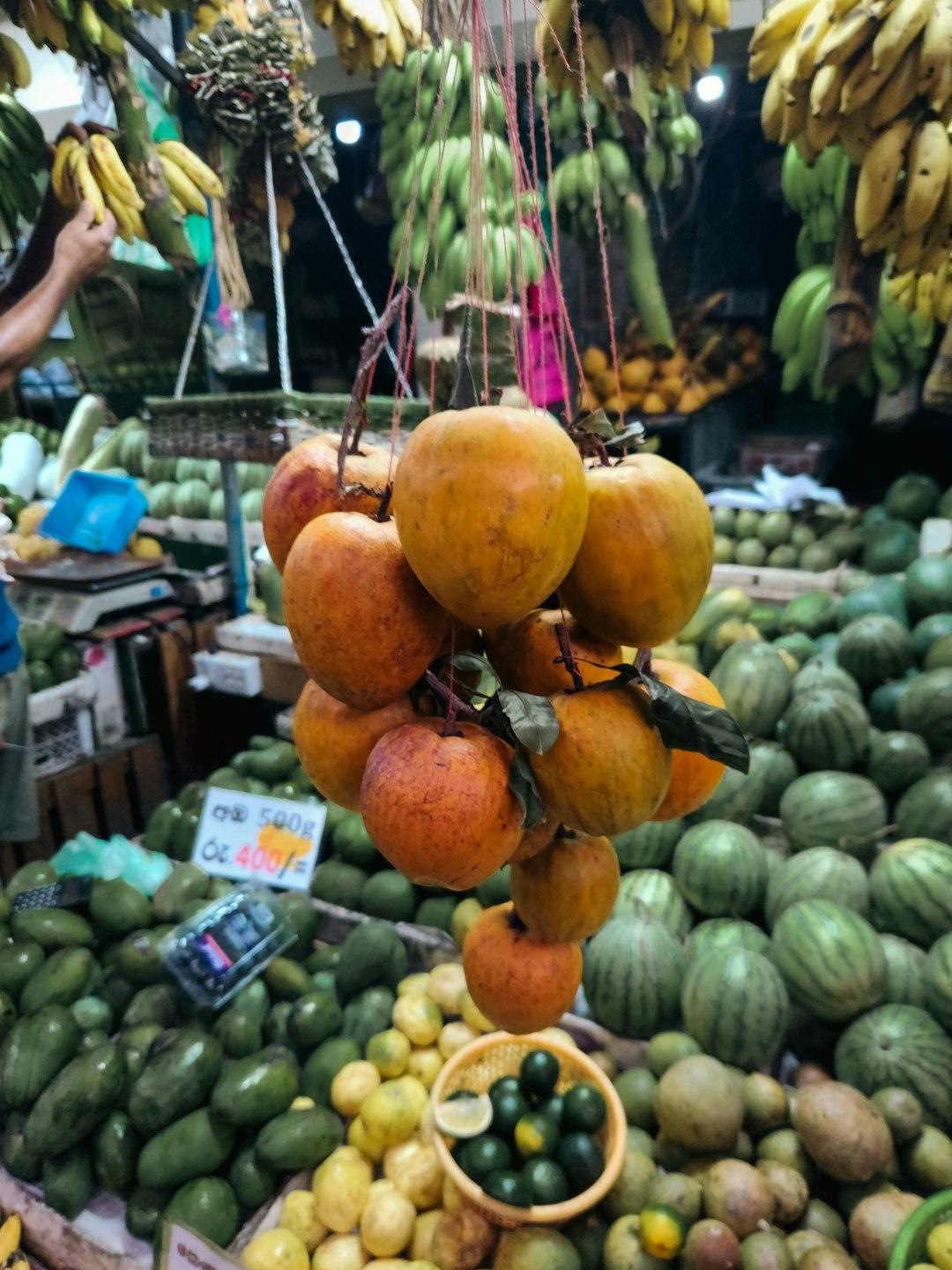 Wiszące pomarańczowe owoce, banany, mango i arbuzy na targu.