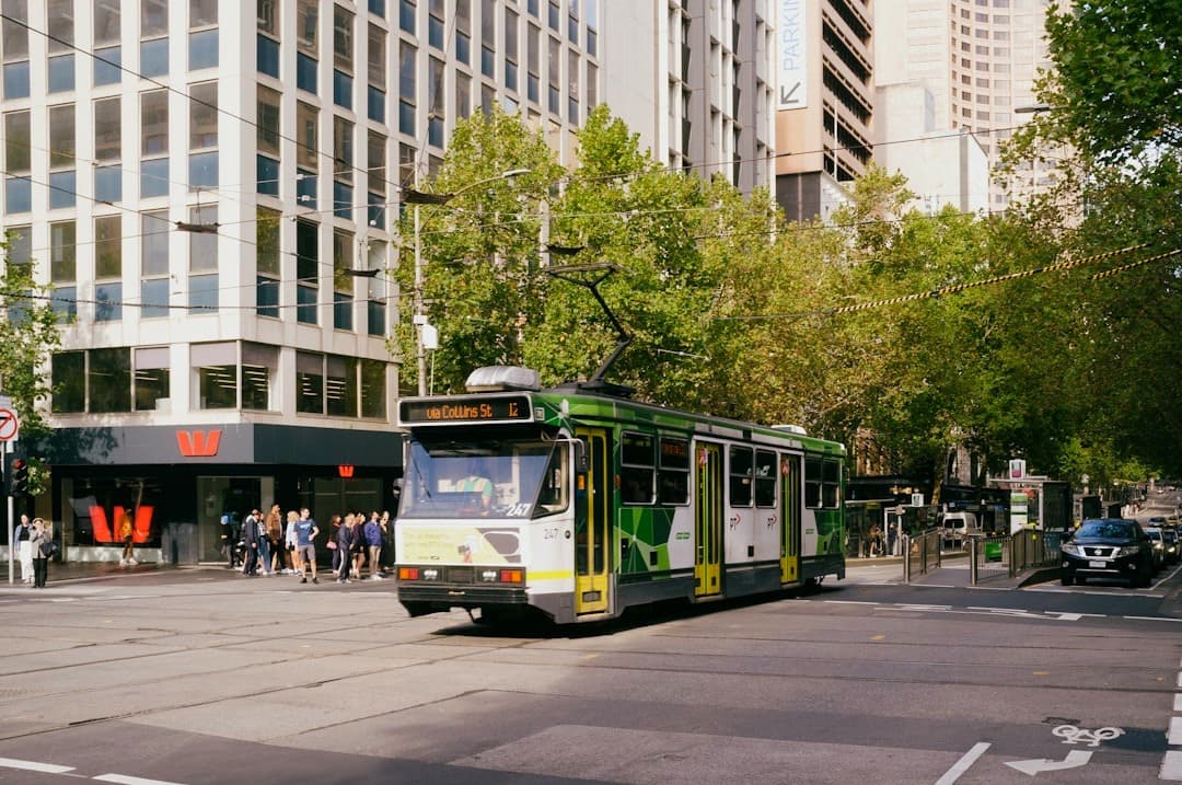Zielony tramwaj na ruchliwej ulicy miejskiej, wysokie budynki, transport publiczny.
