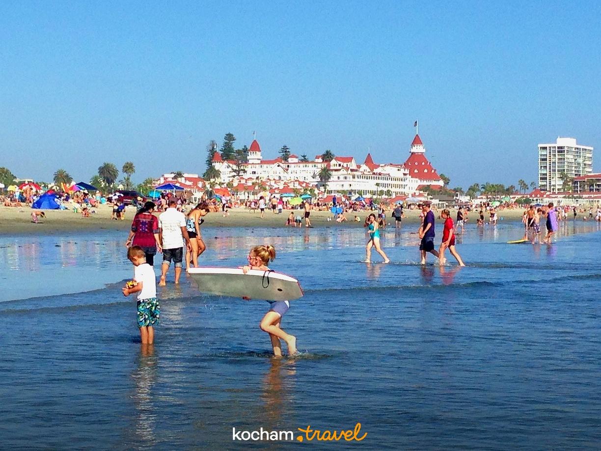 Słoneczna plaża, Hotel del Coronado, kąpiący się ludzie, błękitna woda.