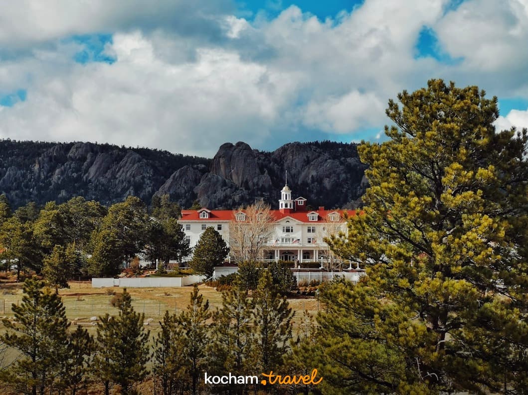 Zabytkowy hotel w górach, otoczony sosnami, pod chmurnym niebem