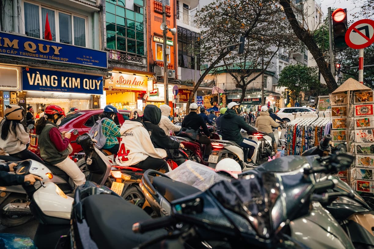 Zatłoczona ulica w Hanoi ze skuterami, ludźmi i szyldami sklepów.