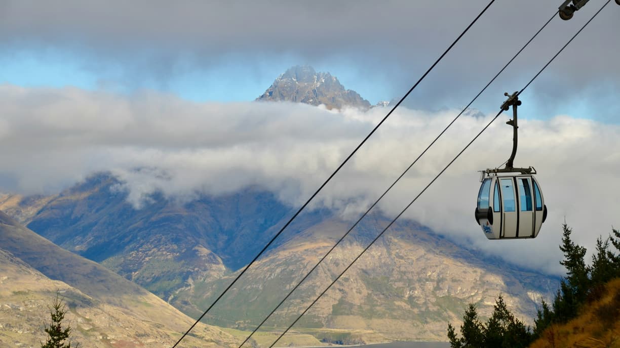 Gondola nad górami, ze szczytem wystającym z chmur.