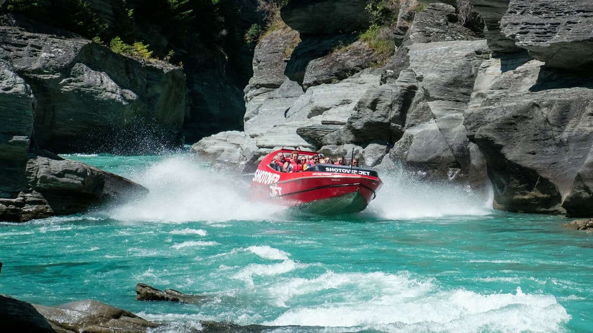 Dynamiczna przejażdżka czerwoną łodzią Shotover Jet po skalistym kanionie.