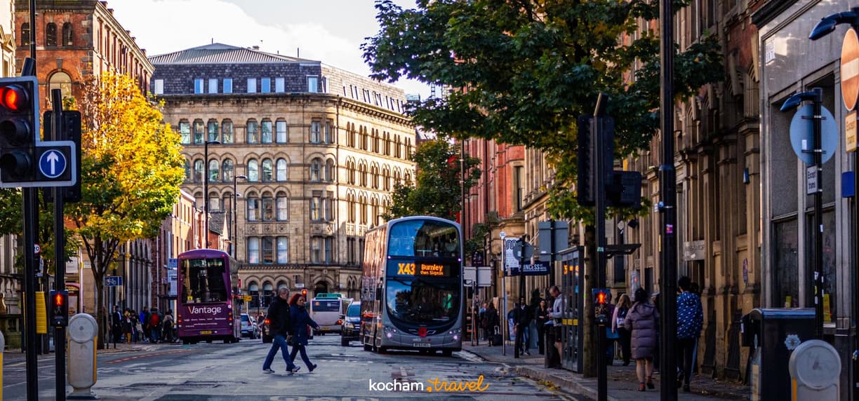 Jesienna ulica Manchesteru z piętrowym autobusem, ludźmi i zabytkowymi budynkami.