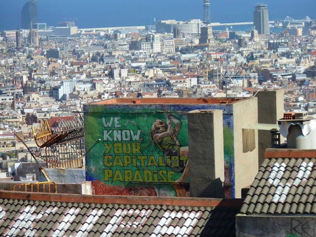 Panoramiczny widok Barcelony z graffiti 'WE KNOW YOUR CAPITALIST PARADISE'.
