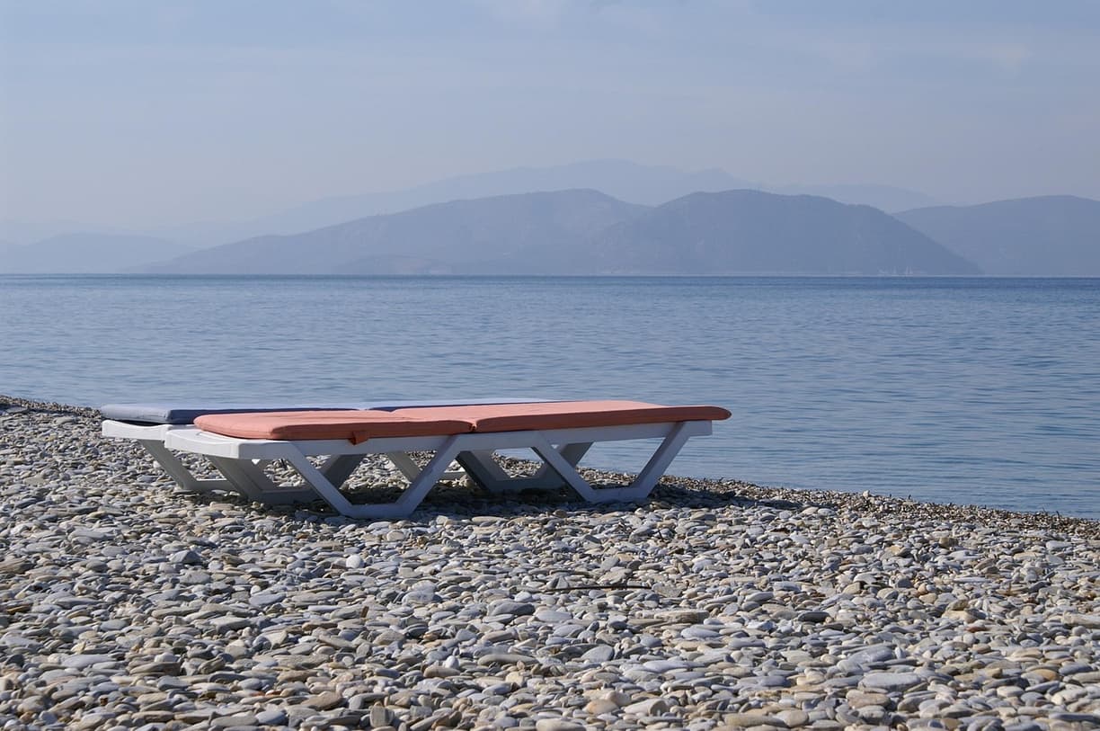 Pusta kamienista plaża z leżakami, spokojnym morzem i odległymi górami.