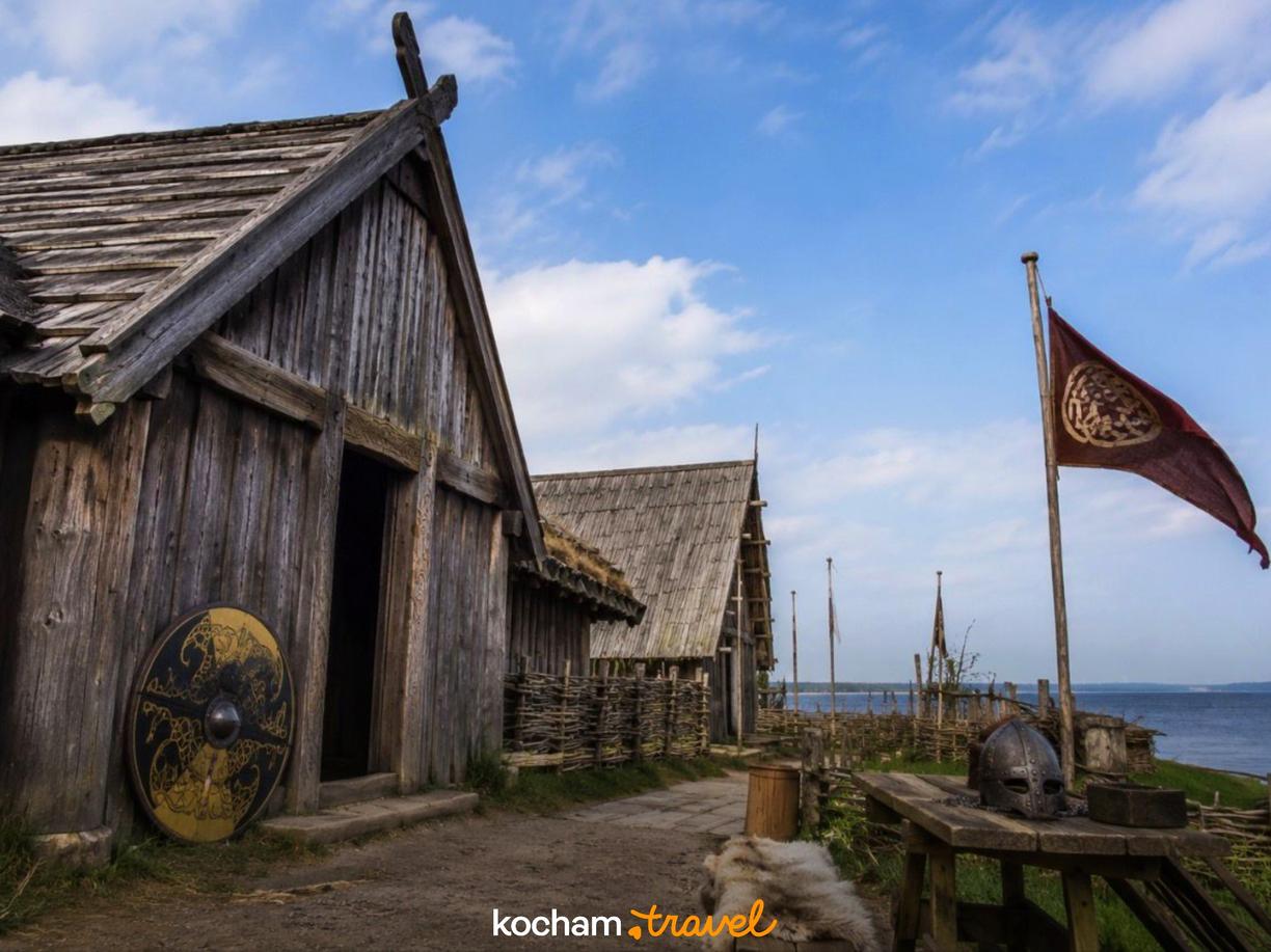 Historyczna osada Wikingów z drewnianymi budynkami, tarczą i hełmem.