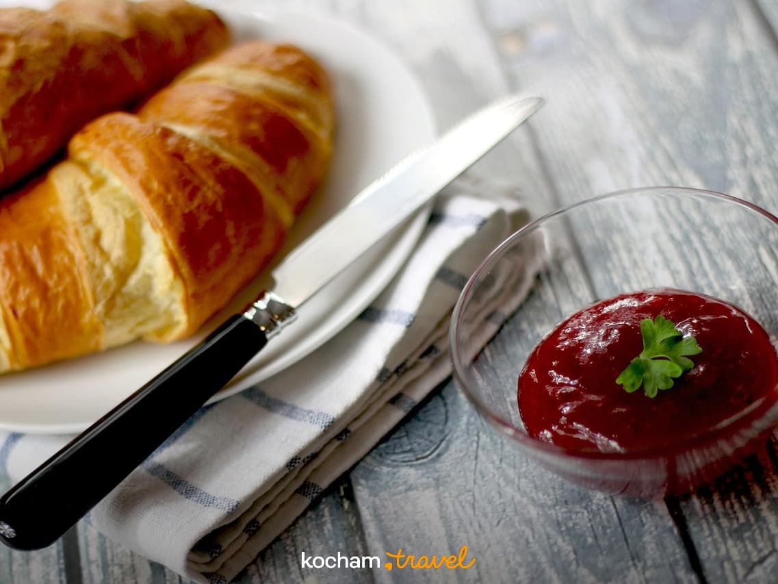 Złote croissanty, dżem, nóż na drewnianym stole – pyszne śniadanie.