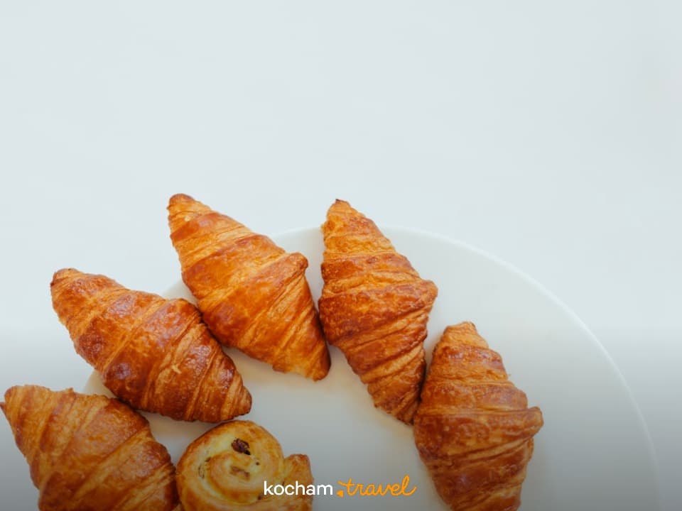 Złociste croissanty i ciastko ślimak na białym talerzu.