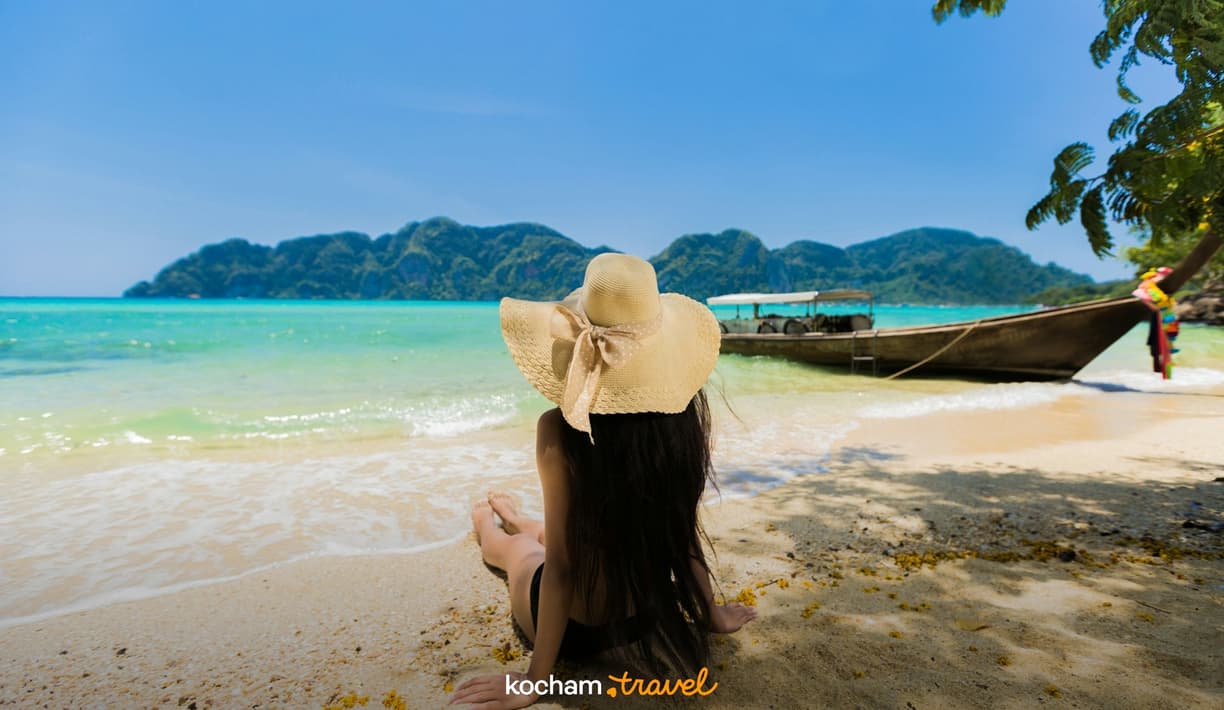 Kobieta w słomkowym kapeluszu na tropikalnej plaży z turkusowym morzem.