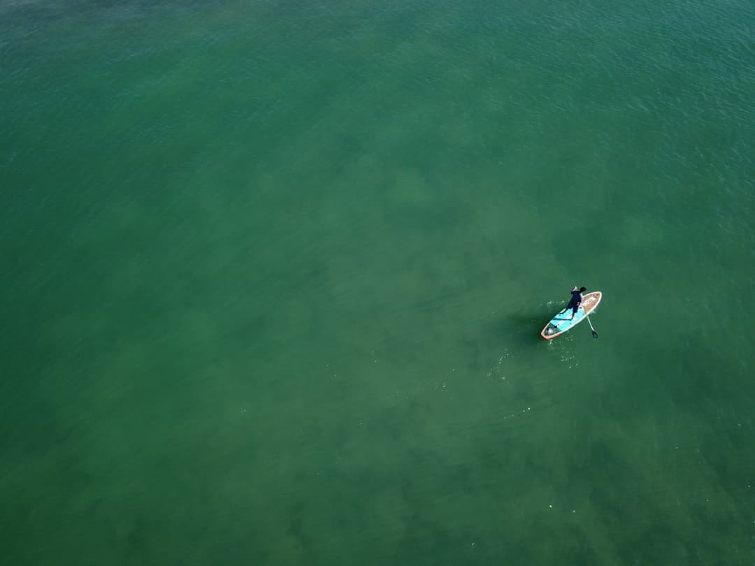 Osoba na desce SUP wiosłująca po spokojnych zielonych wodach oceanu.