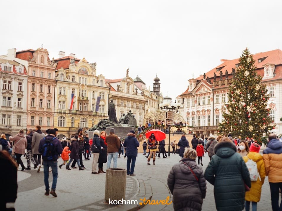 Tłum na historycznym placu miejskim z choinką i starymi budynkami.