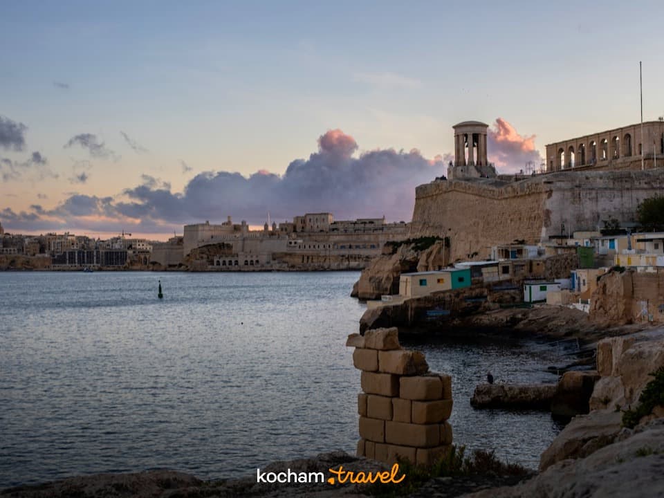 Valletta, Malta: historyczne fortyfikacje, dzwonnica i wybrzeże o zachodzie słońca.