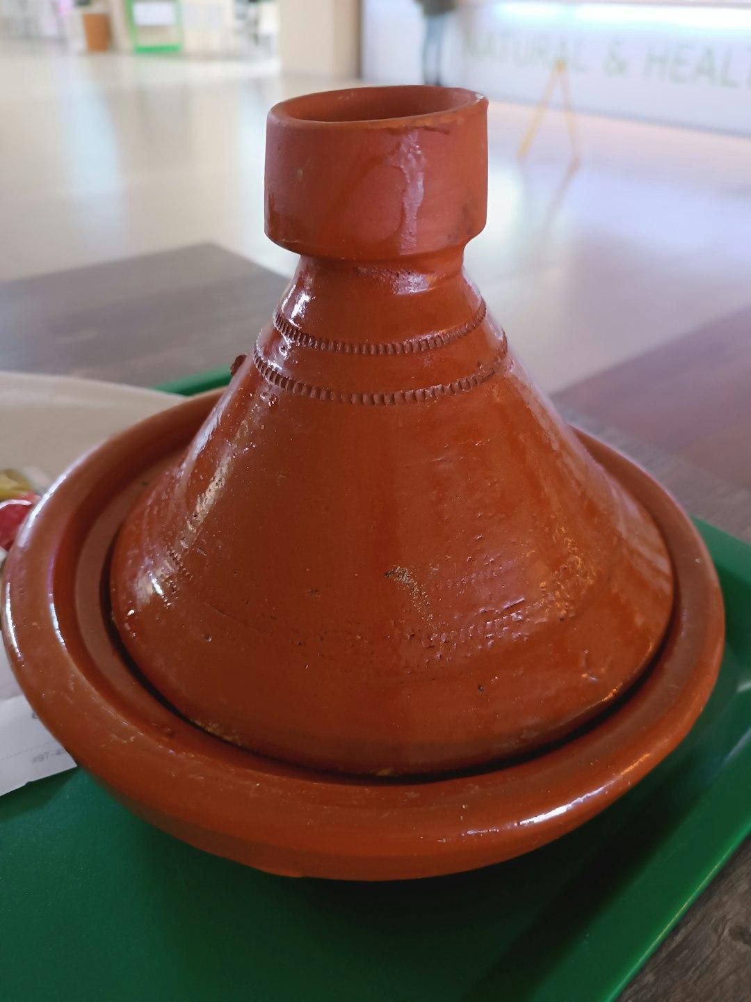 Gliniany tagine z stożkową pokrywką na zielonej tacy.