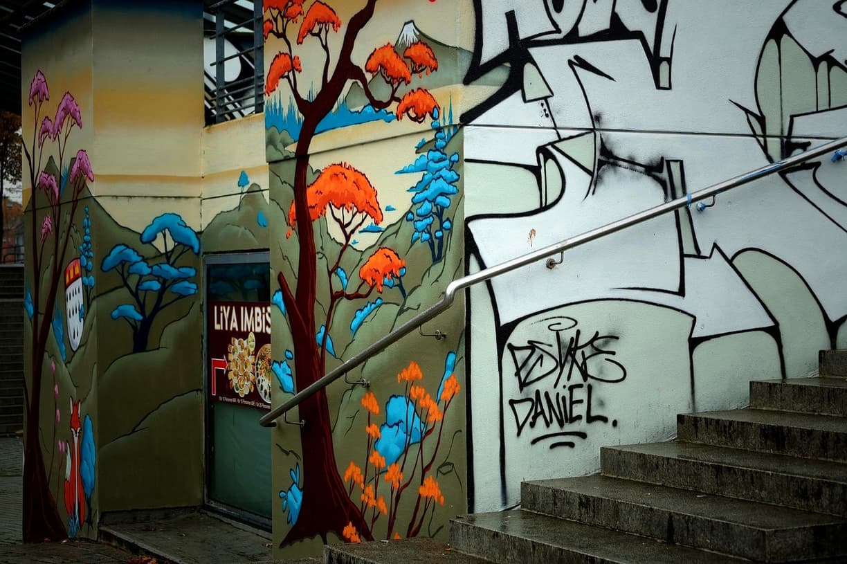 Kolorowy mural i abstrakcyjne graffiti na ścianie miejskiego budynku ze schodami.