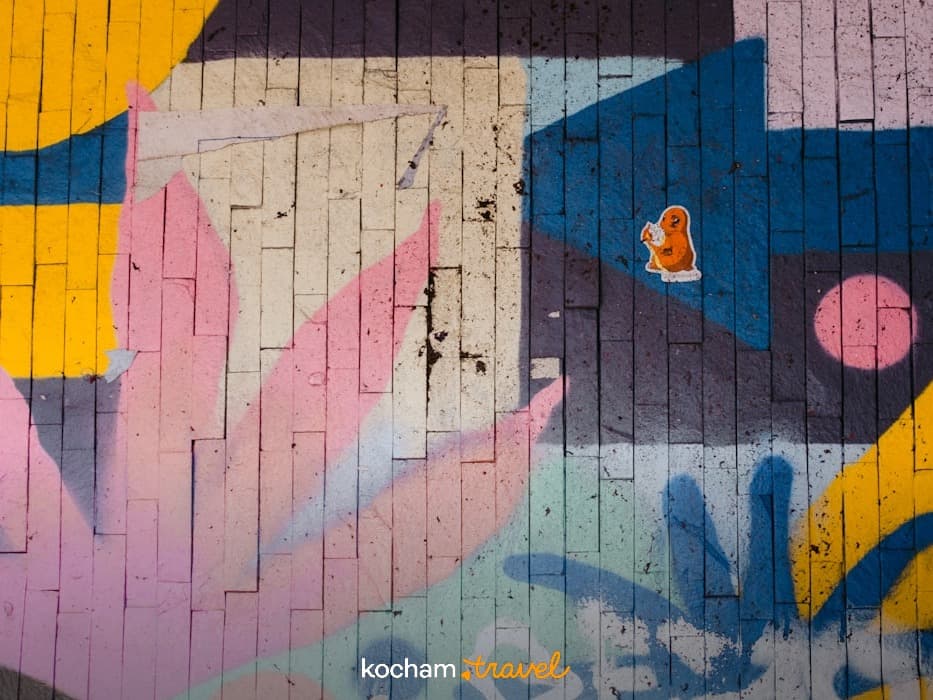 Żywe, abstrakcyjne graffiti na ceglanej ścianie z naklejką, miejska sztuka.