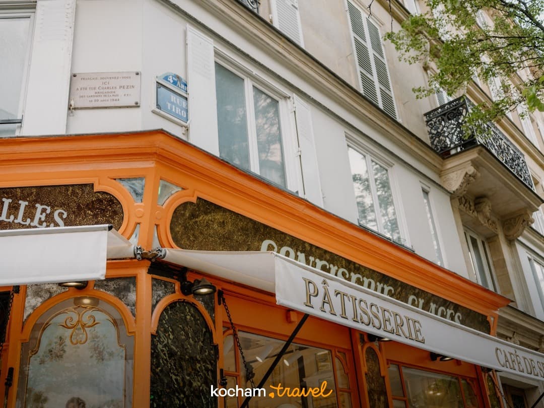 Paryska patisserie z pomarańczową fasadą i klasyczną architekturą miejską.