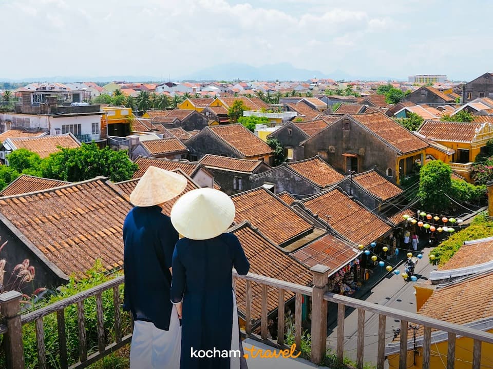 Ludzie w stożkowych kapeluszach podziwiają panoramę starego miasta Hoi An.