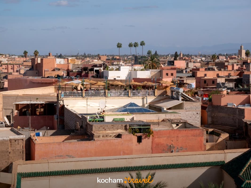 Słoneczna panorama dachów Marrakeszu z różowymi budynkami i palmami.