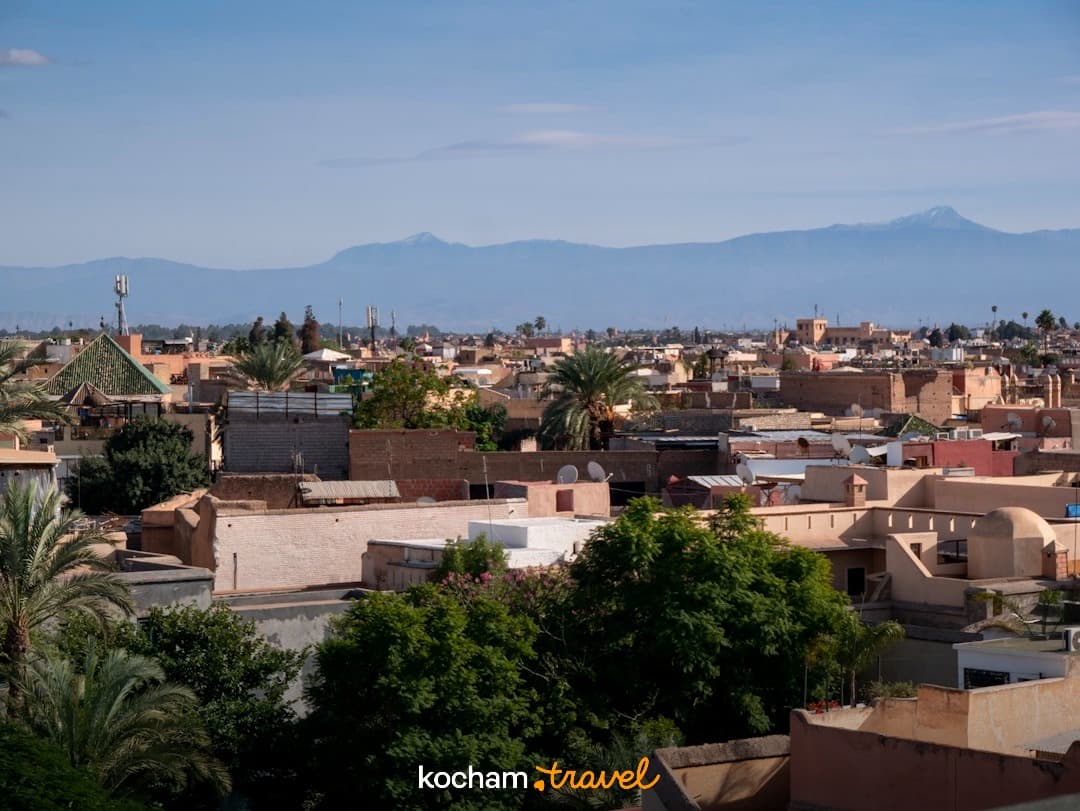 Panoramiczny widok na dachy Marrakeszu z ośnieżonymi górami Atlas w tle.