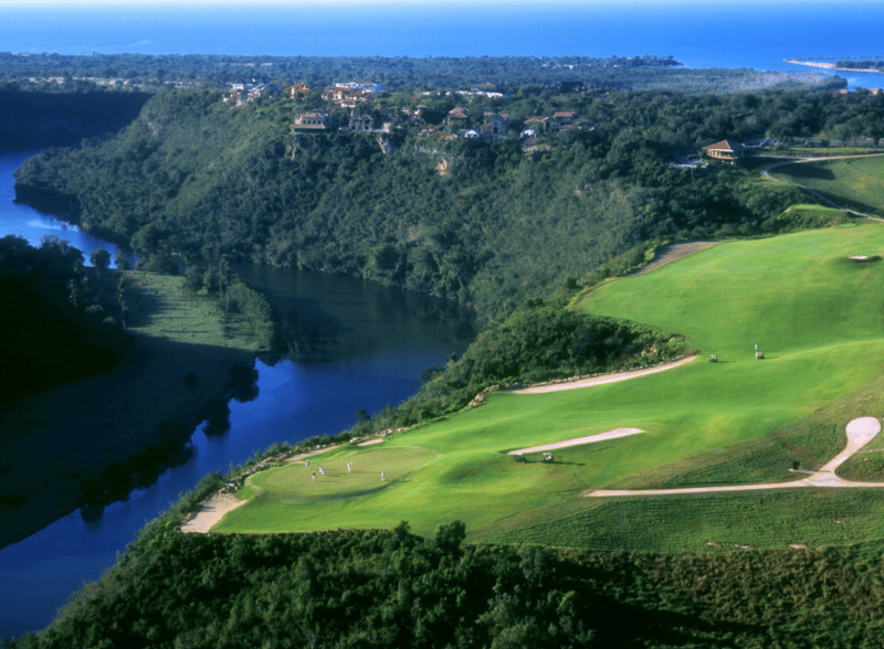 Pola golfowe nad rzeką, zielone wzgórza i ocean.