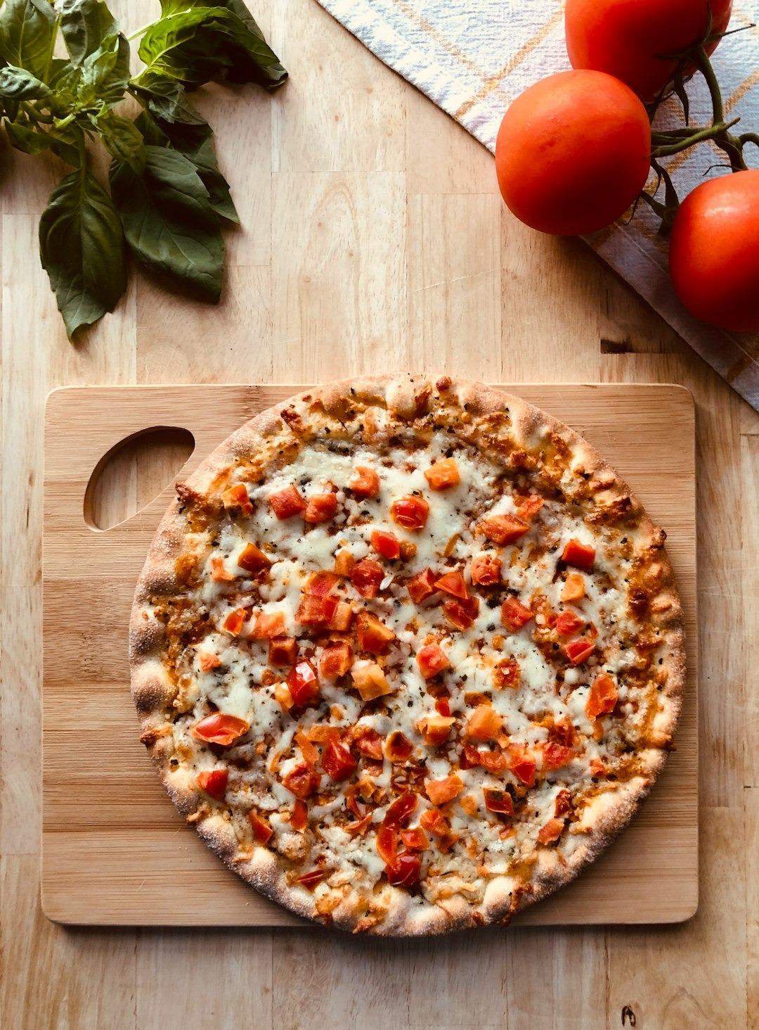 Świeża pizza z serem, pomidorami i bazylią na drewnianym stole.