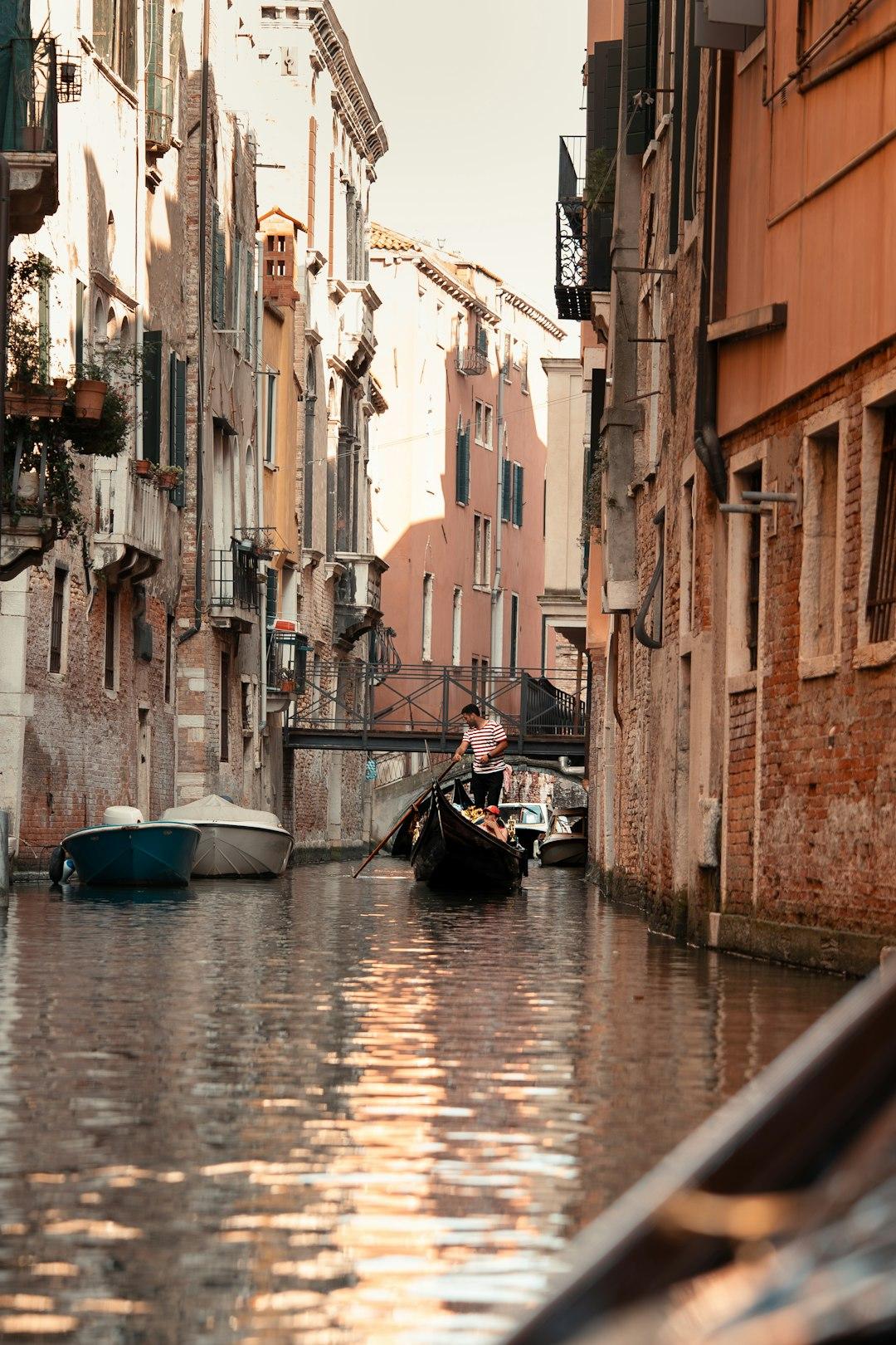 Gondola z gondolierem i turystami na wąskim weneckim kanale.