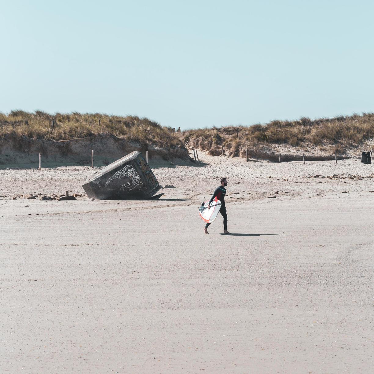 Surfer idący po piaszczystej plaży w słoneczny dzień.