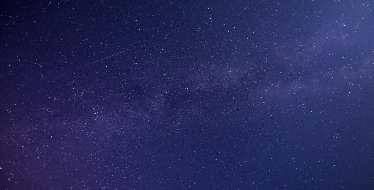 Gwieździste nocne niebo z widoczną Drogą Mleczną i spadającymi gwiazdami.
