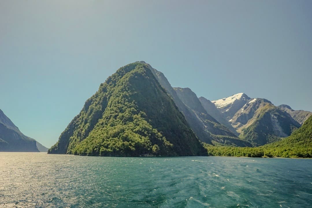 Malowniczy fiord, zielone góry, turkusowa woda, ośnieżone szczyty.