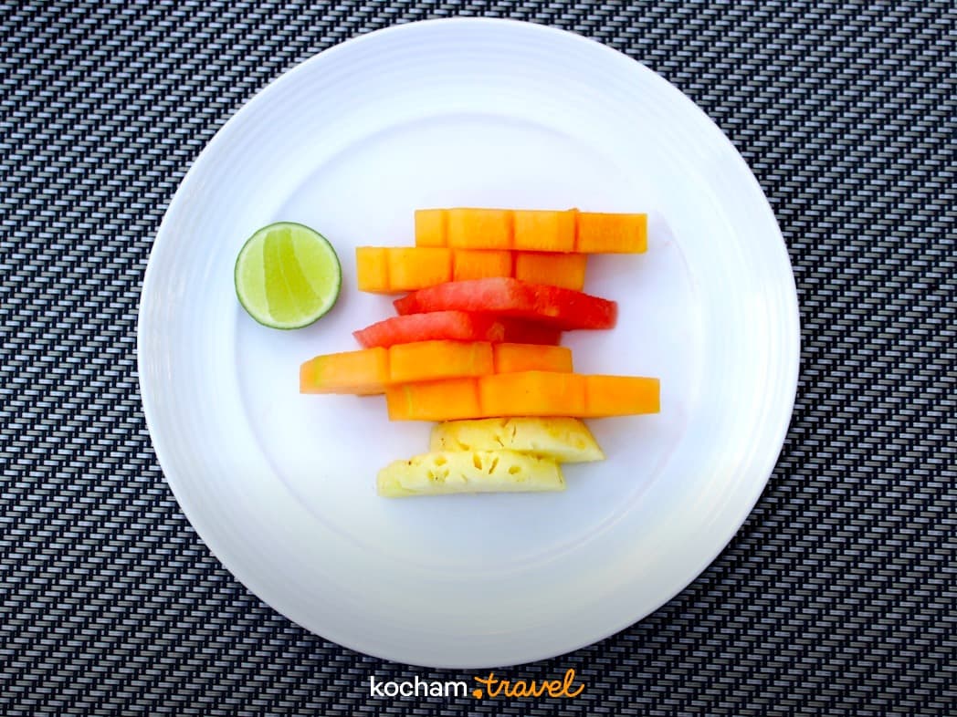 Kolorowe świeże owoce tropikalne: melon, arbuz, ananas i limonka na talerzu.
