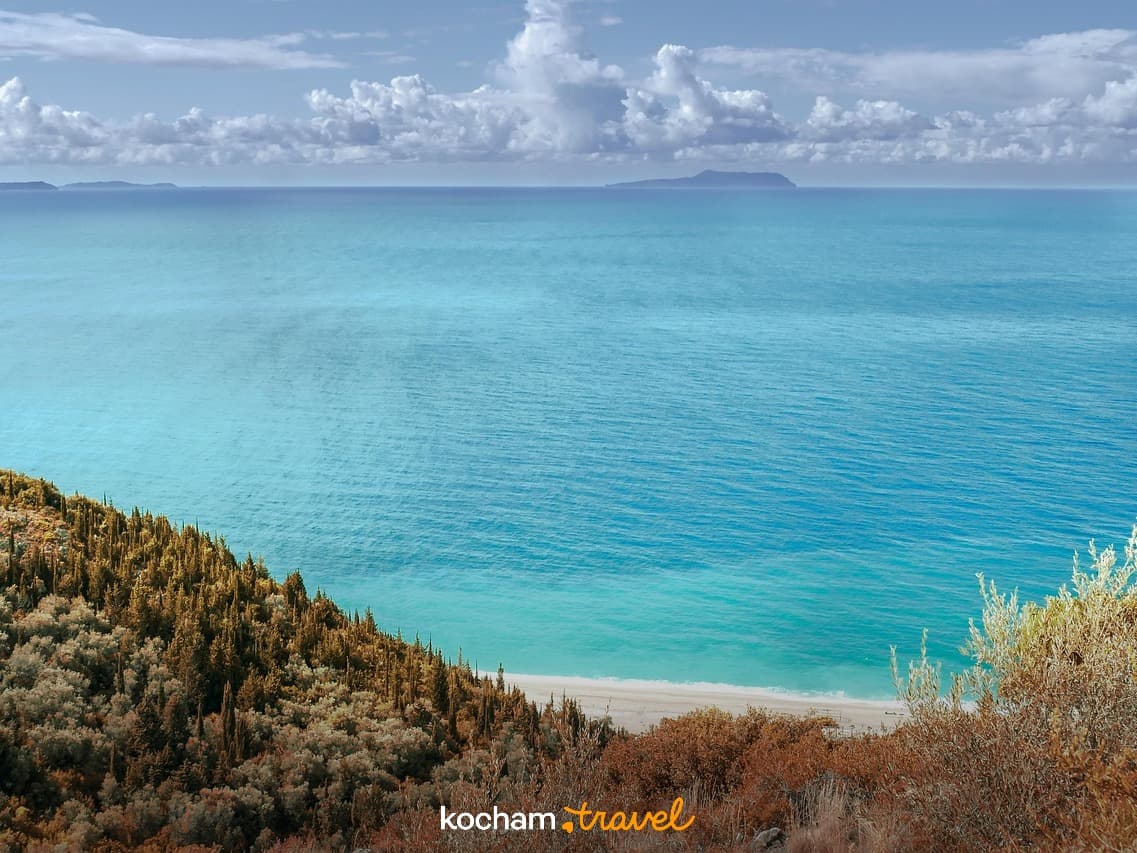 Panoramiczny widok na turkusowe morze, piaszczystą plażę i zalesione wybrzeże.