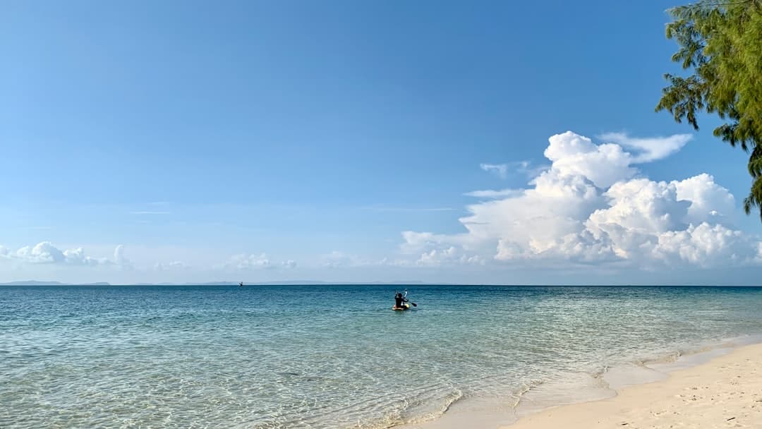 Plaża, kajakarz na oceanie pod niebem.