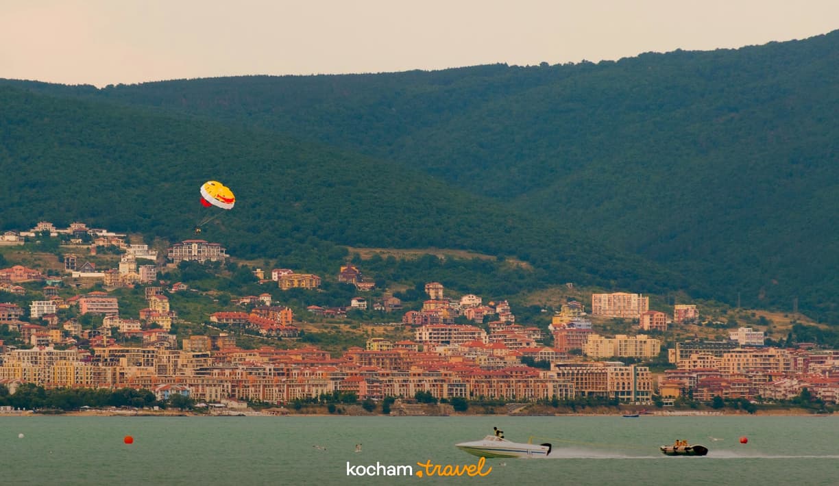 Kurort nadmorski z domami na wzgórzach, parasailing i motorówki.