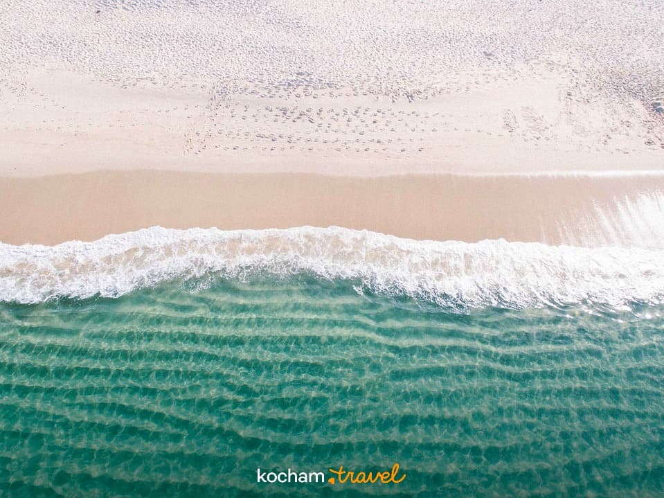 Biała piaszczysta plaża, turkusowy ocean, delikatne fale, widok z góry.