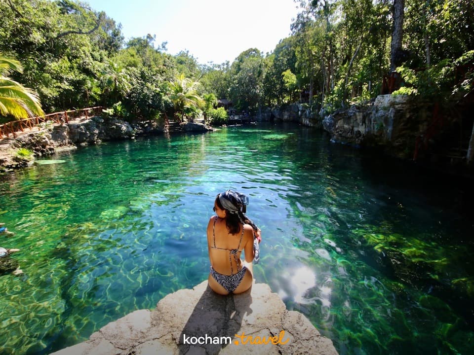 Kobieta w bikini nad turkusowym naturalnym basenem w dżungli.