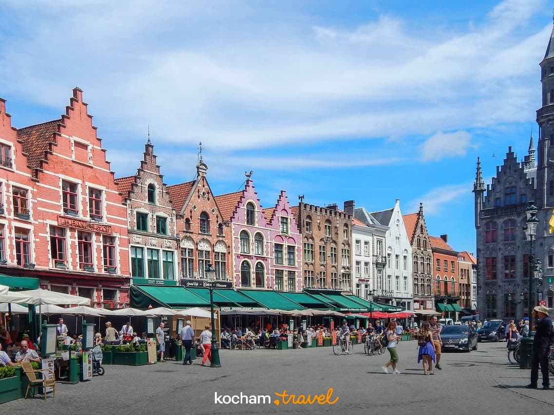 Tętniący życiem rynek Brugii z zabytkowymi budynkami i kawiarniami na świeżym powietrzu.