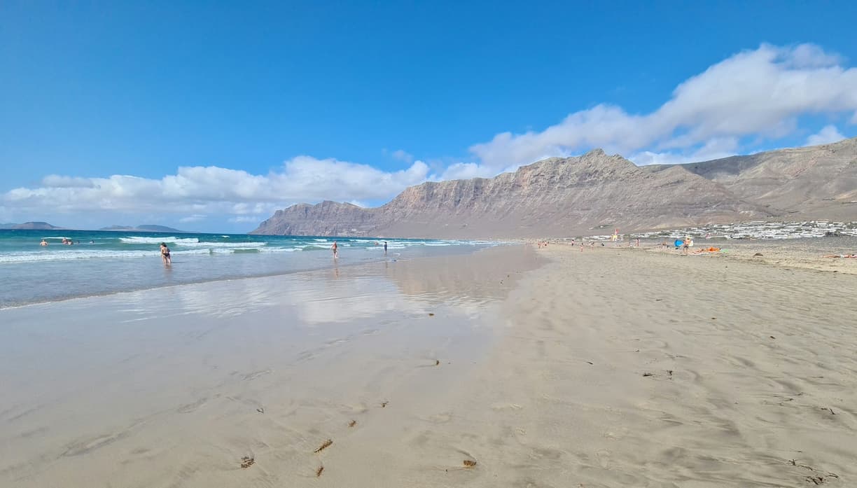 Plaża z turkusowym morzem i górami w tle.