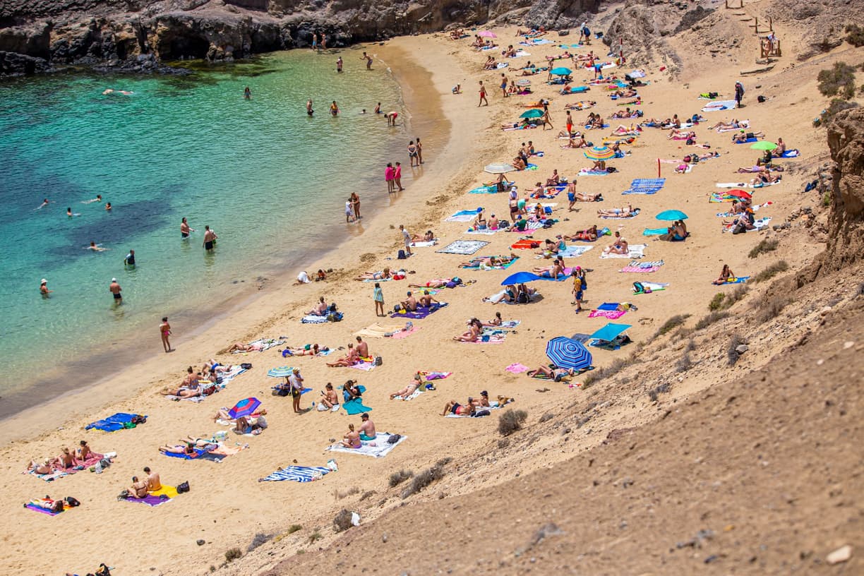 Turyści odpoczywający na piaszczystej plaży z turkusowym morzem.